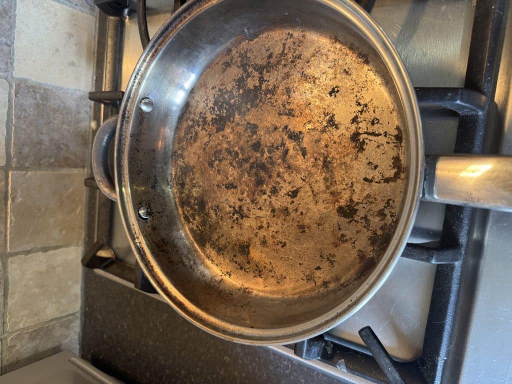 Stainless steel frying pan with food burnt on after cooking over a campfire