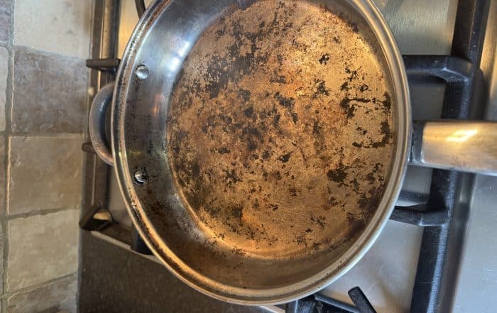 Stainless steel frying pan with food burnt on after cooking over a campfire